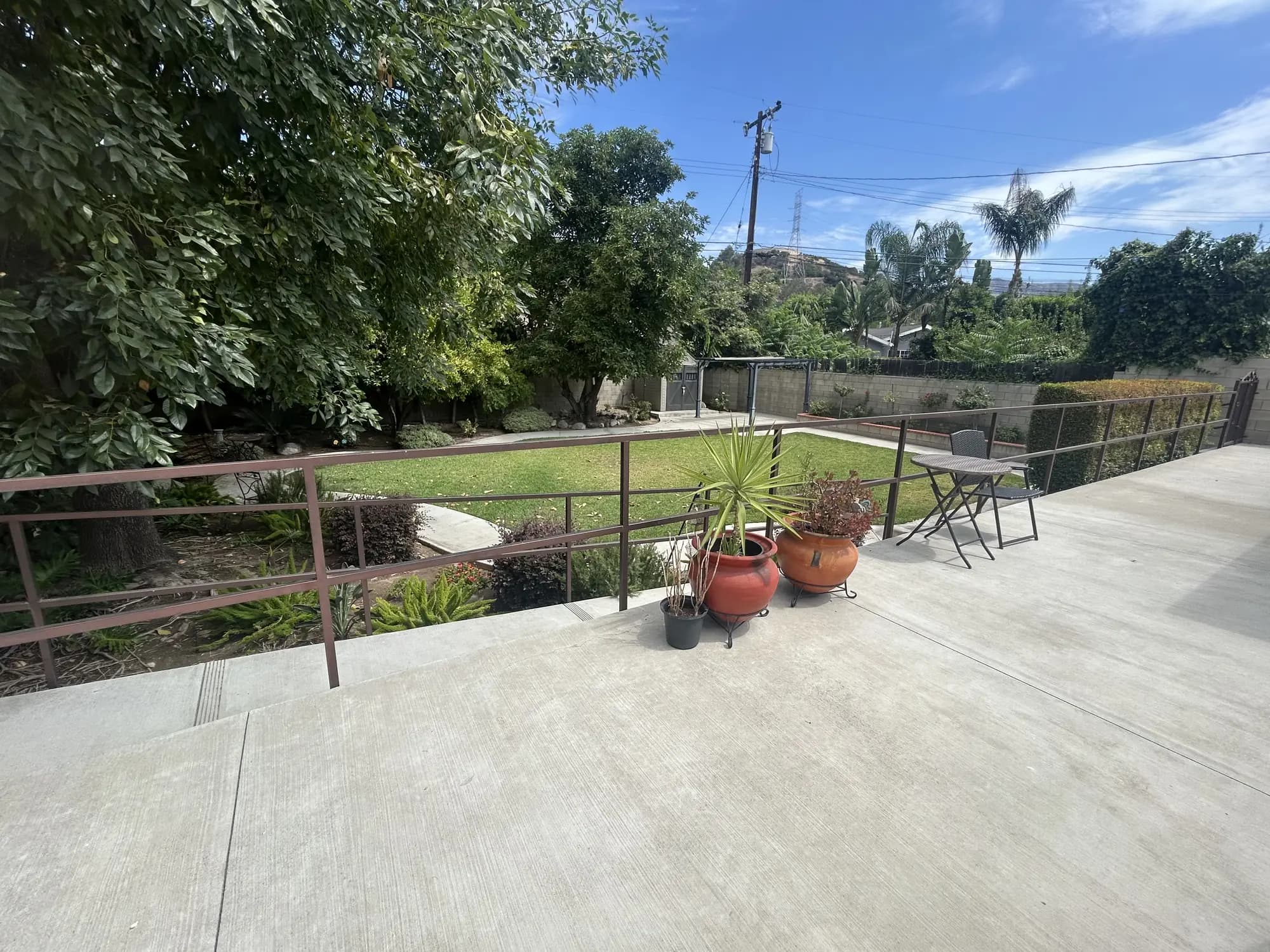 Outdoor patio and landscaped garden at Bradford Residential Care with lawn, mature trees, potted plants, railing, and outdoor seating