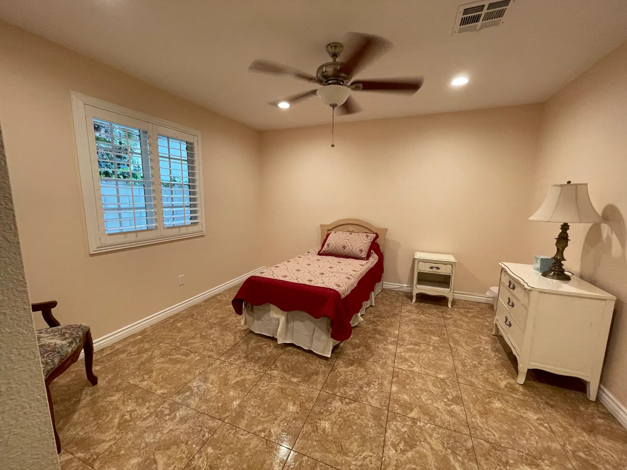A single-resident bedroom at Bradford Residential Care with one bed, a nightstand, a dresser, and a shuttered window